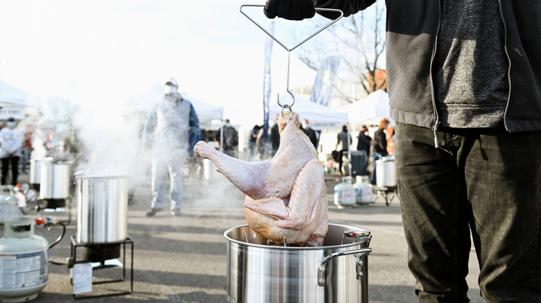 someone loads a full turkey into a fryer