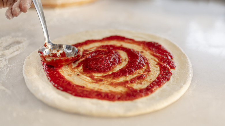 person adding sauce to pizza dough