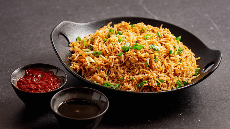A bowl of egg-fried rice with two ramekins, one of soy sauce and one of sriracha