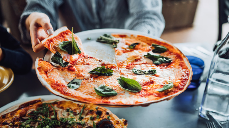 Someone holding a plate of pizza Margherita and taking a slice.