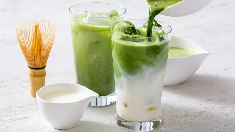 Two iced matcha lattes and a bamboo whisk.