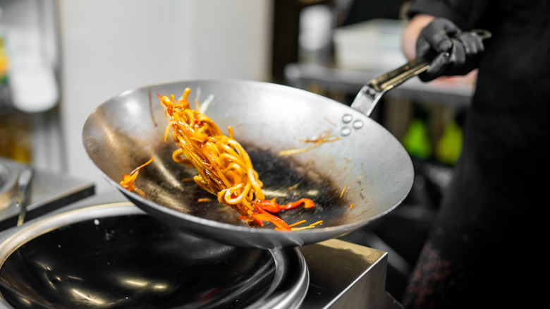 chef tossing noodles in wok